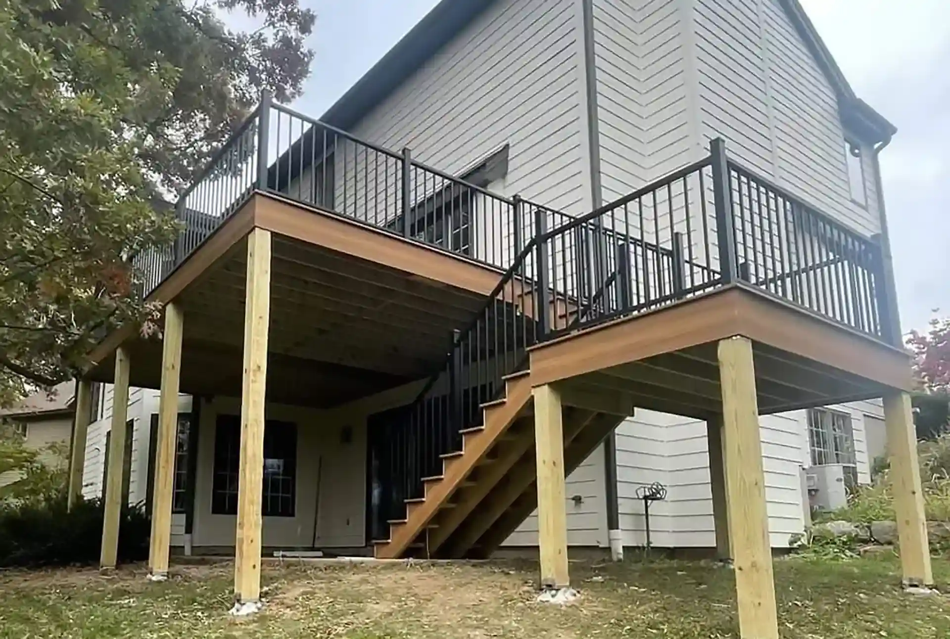 PHoto of an elevated deck with black metal railing, and steps leading down to a patio below. The steps include a platform and lead to the dryspace below the deck.
